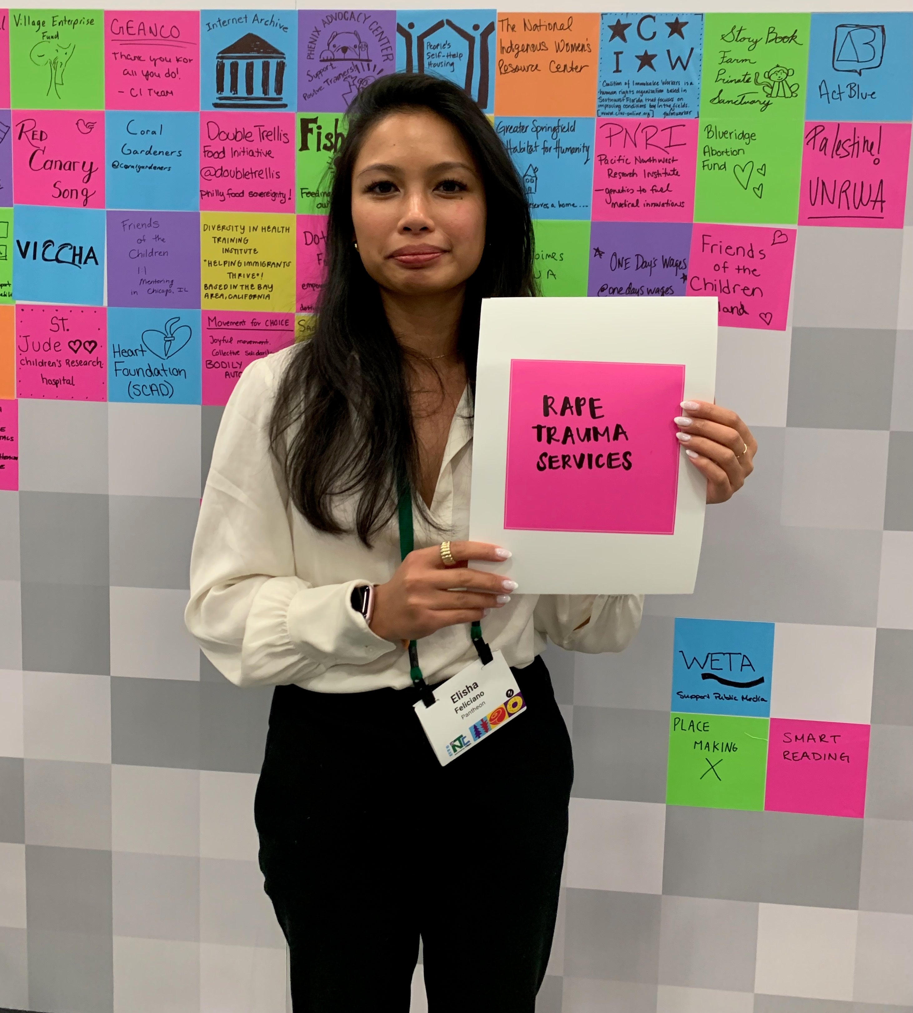 Elisha Feliciano, an Asian woman with long brown hair holding a sign with her favorite nonprofit cause 'Rape Trauma Services'
