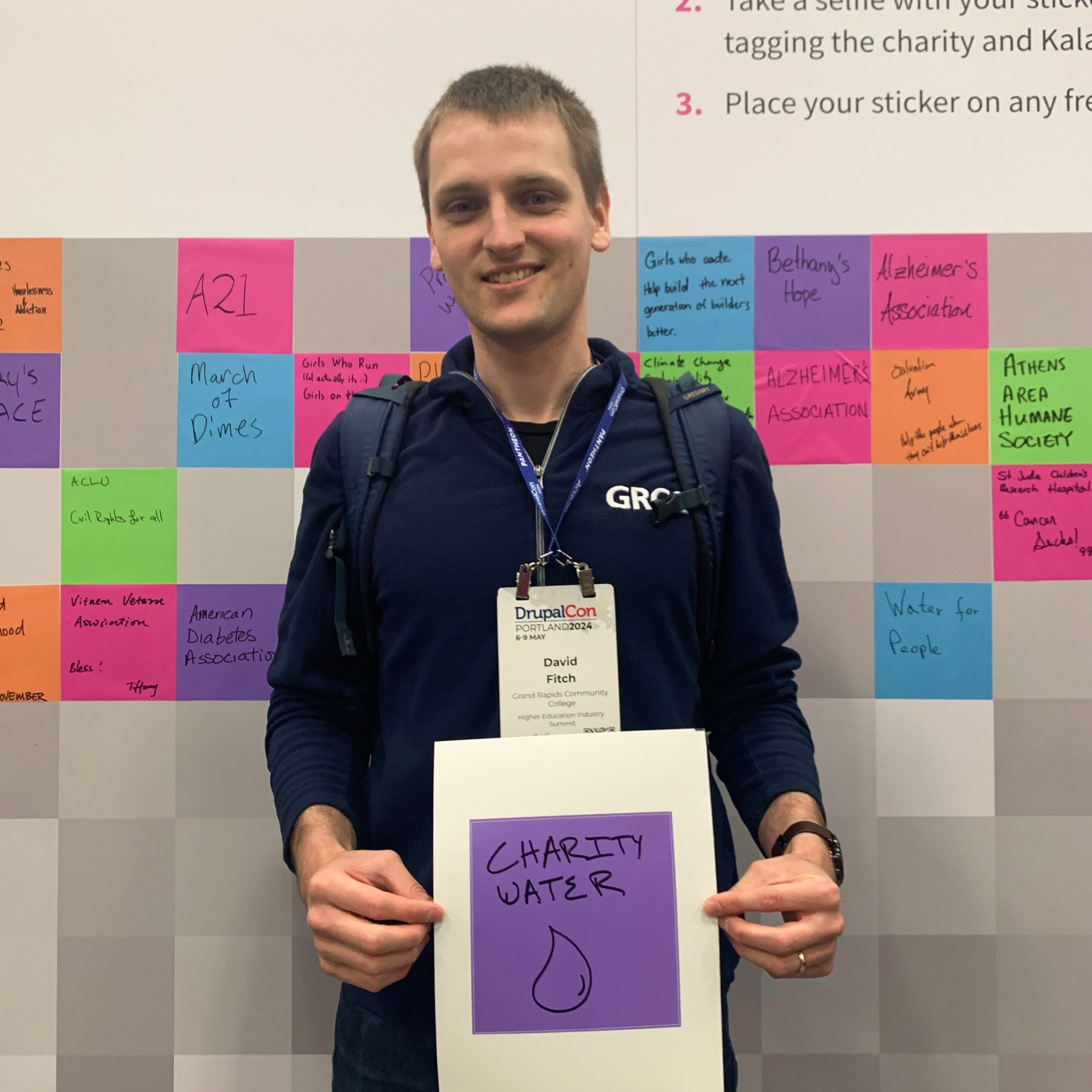 David Fitch holds a purple square sticker with "Charity Water" written on it and a water droplet below the text.