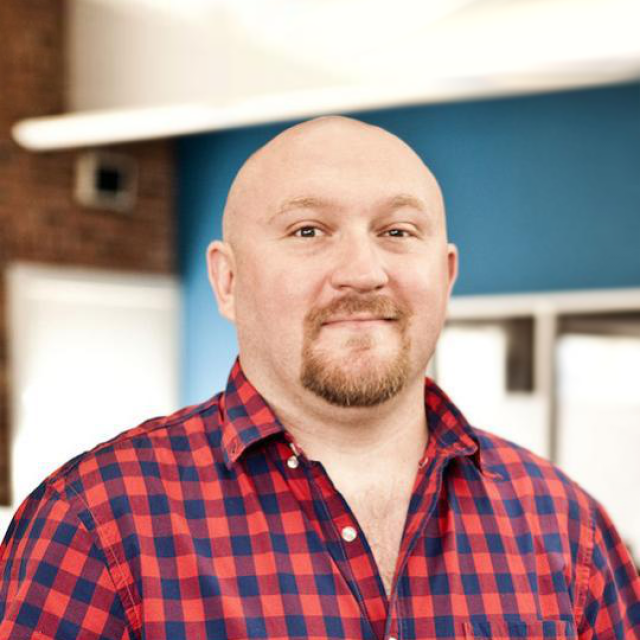 David smiles at the camera in a plaid collared shirt.