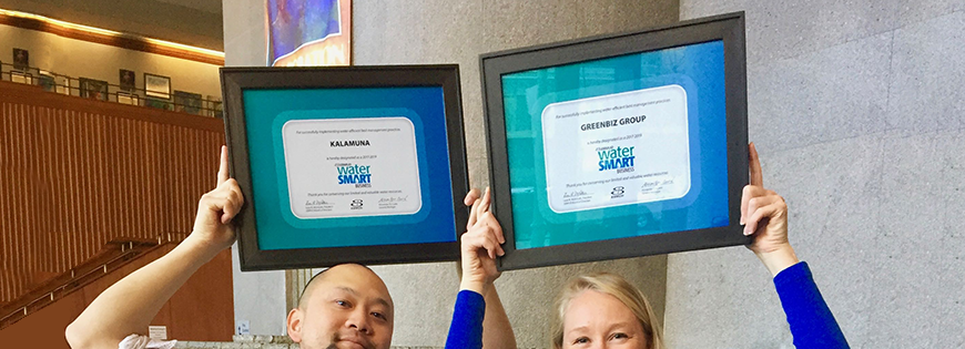 Two people hold up green business certificates