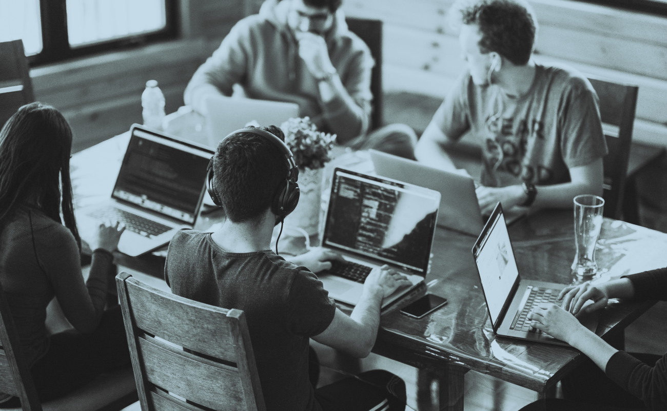 Group of four people working on computers at a table. 